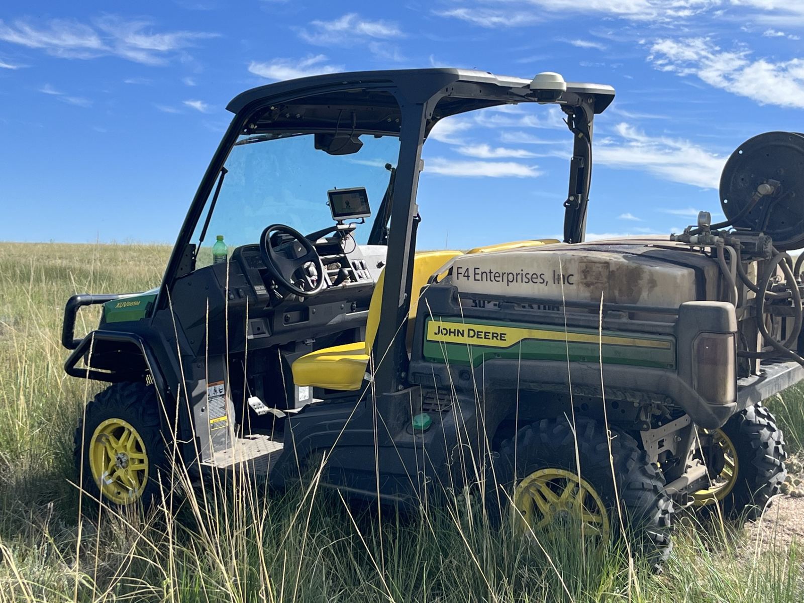 The F4 Enterprises John Deere Gator sprayer with GPS guidance, parked in tall pasture grass
